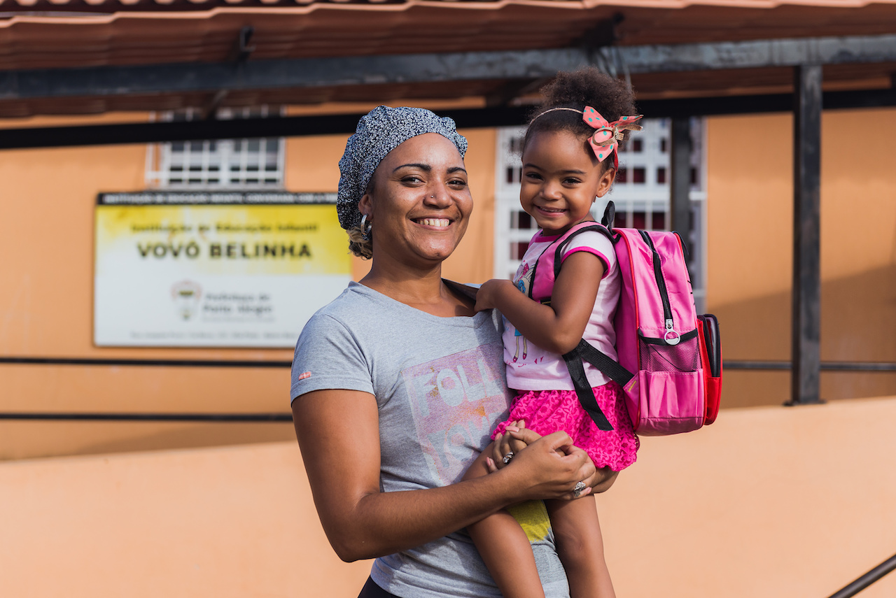 Mulher com uma criança no colo. Ambas sorriem.