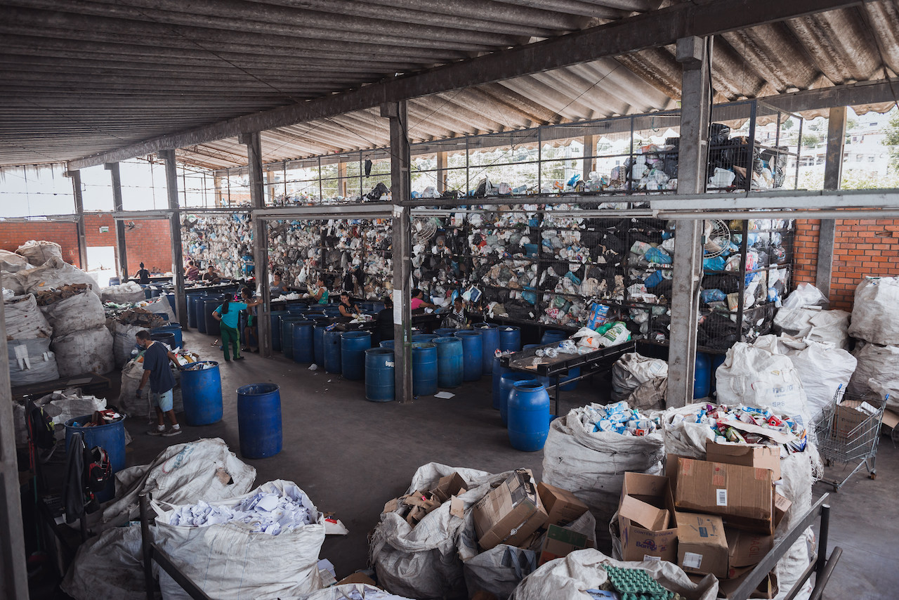 Imagem do centro de triagem, com pilhas de material para reciclagem e pessoas trabalhando